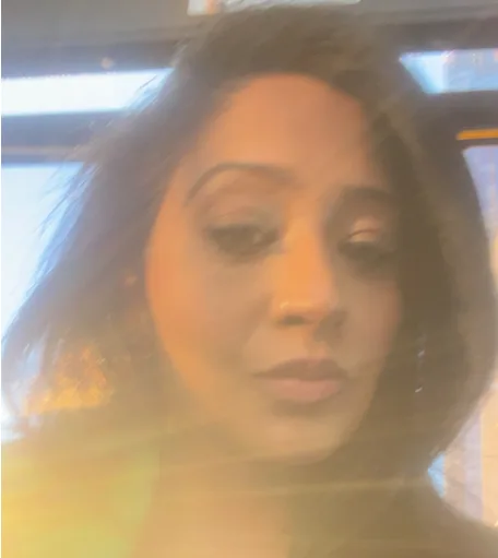 Woman with dark wavy hair in soft natural light with golden sun flare washing over the image, creating a dreamy, reflective mood