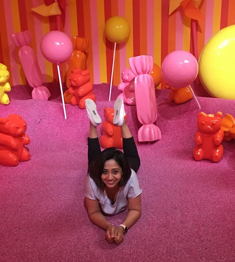 A woman smiling while lying on a pink floor in a colorful candy-themed room, representing the joy and freedom that can come from career transitions and successful job searching.